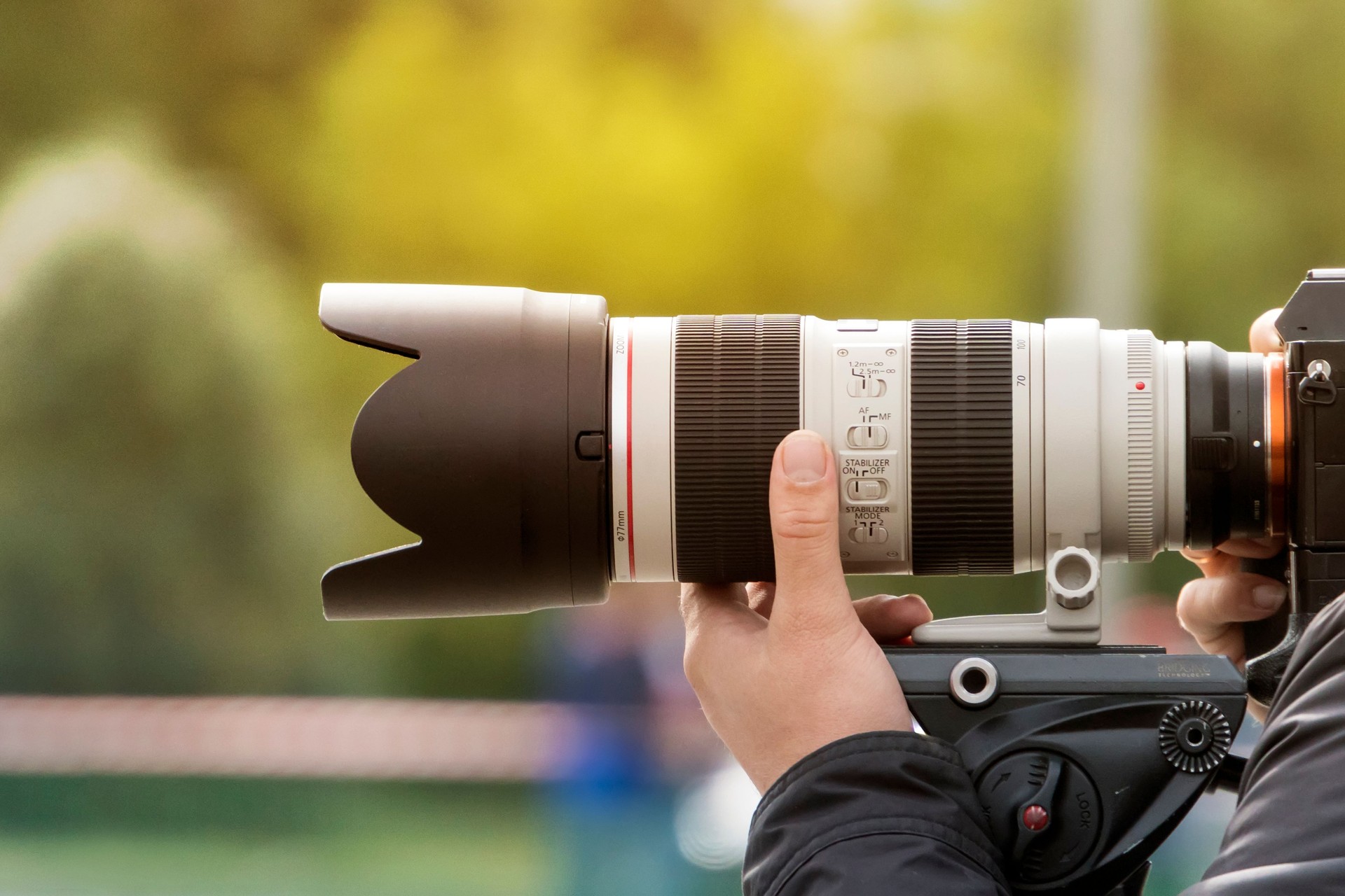 Handshot of a professional photographer outdoors. Man holds a modern camera device. Cameraman shoots outdoors. Shooting with lens. Paparazzi with high-end optical objective. Photographic equipment