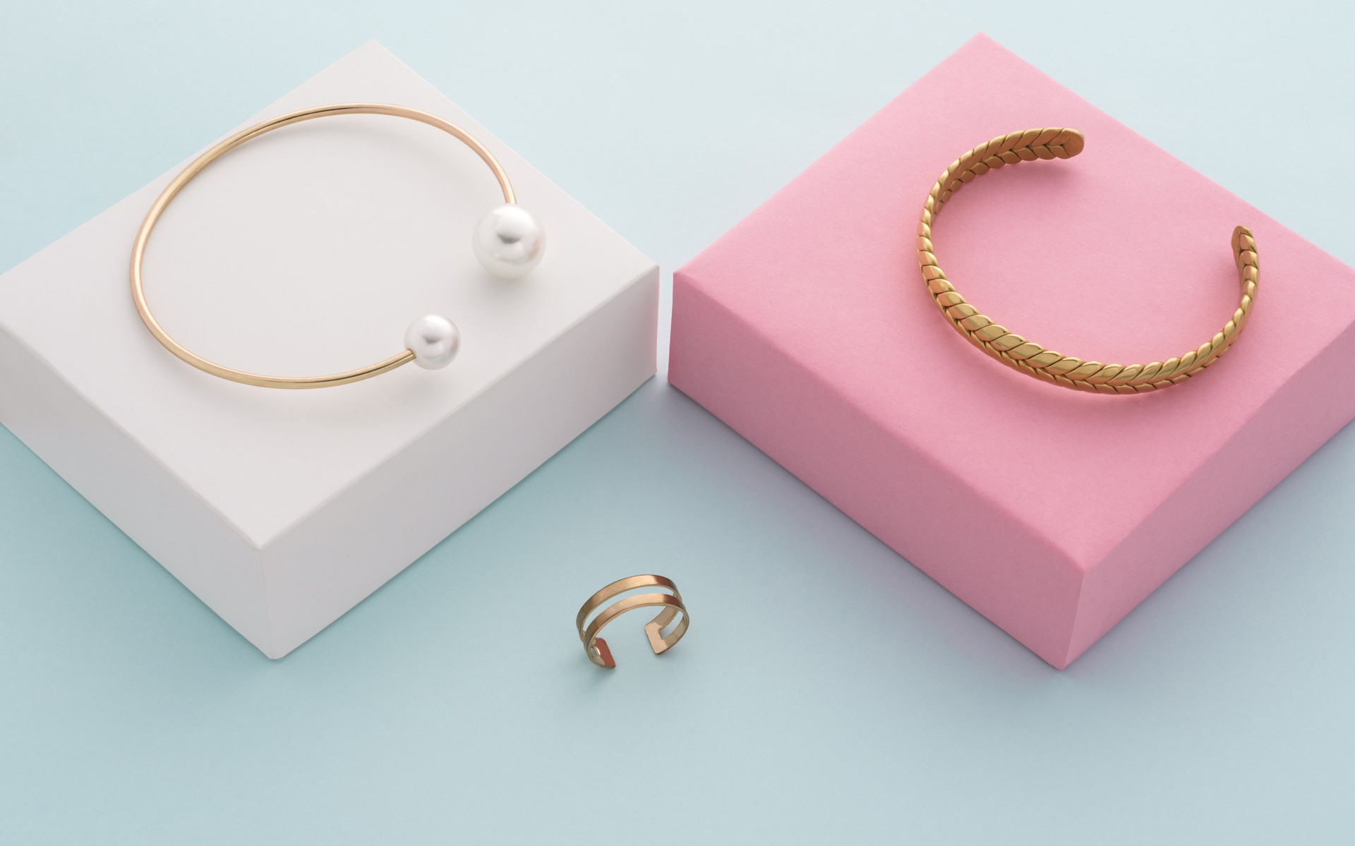 Modern golden bracelets on pink and white boxes and double shape ring on blue background